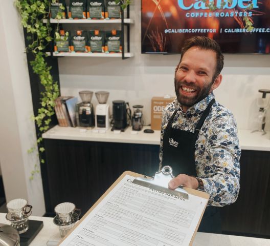 A Caliber Coffee Employee Holding Out A Tasting Menu