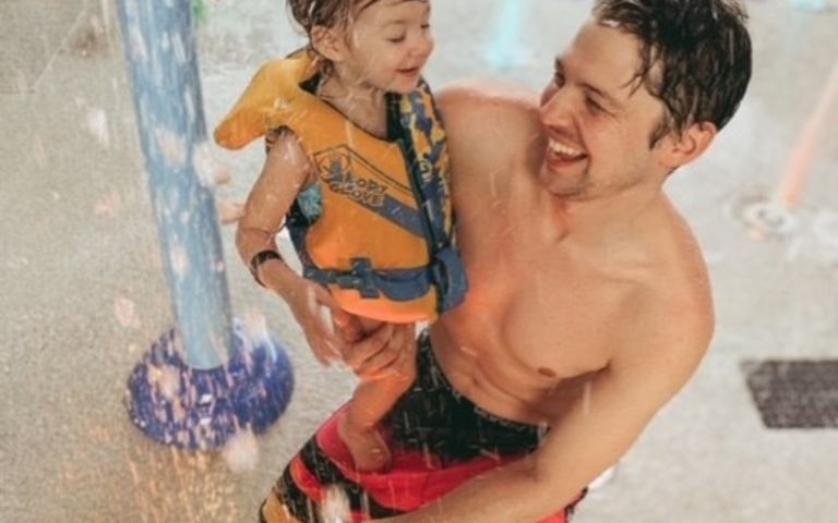 Father in a bathing suit playing with his daughter in a Body Glove vest at Soaked! Waterpark